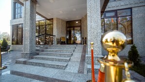 A building entrance with granite steps leading to a door, a red rope barrier, and a golden trophy on display. - Discovery Hotel (Bishkek)