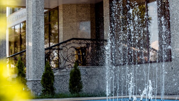 A fountain with multiple water jets in front of a building with a stone facade and a balcony. - Discovery Hotel (Bishkek)