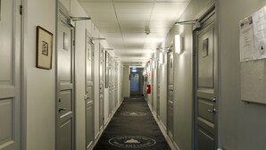 A hotel corridor with doors on both sides, a fire extinguisher, and a carpet with a logo. - Gripsholms Bed & Breakfast (Mariefred)