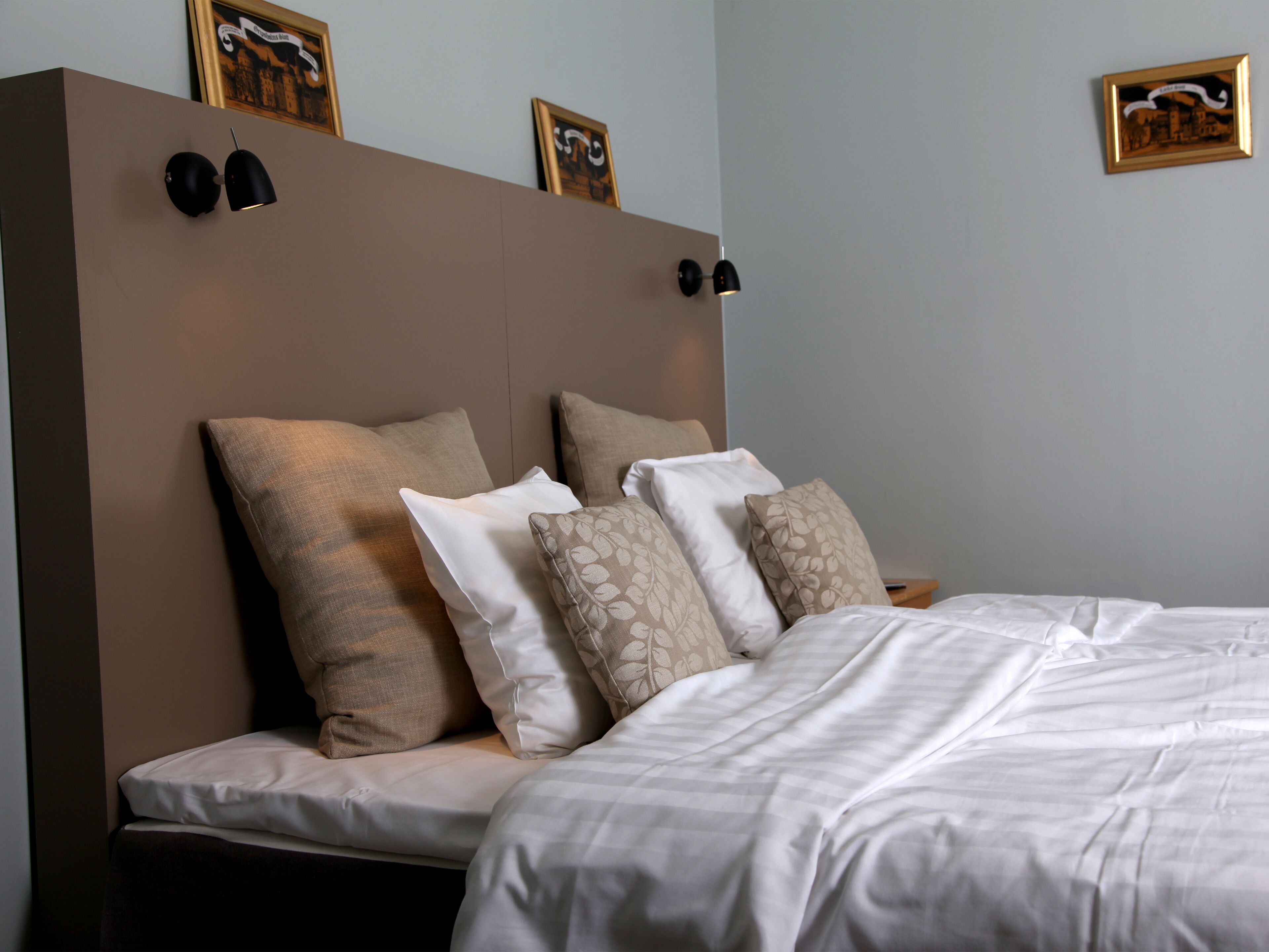 Una cama bien hecha con cabecera, varios almohadones y lámparas fijadas a la pared.