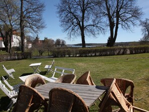 An outdoor seating area with wicker chairs and a wooden table, overlooking a lake and trees. - Gripsholms Bed & Breakfast (Mariefred)