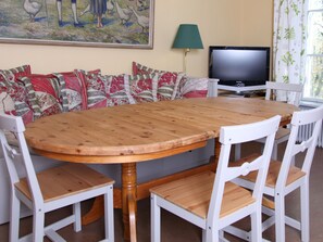 A dining area with a wooden table and white chairs, a sofa with patterned cushions, a television, and a lamp. - Gripsholms Bed & Breakfast (Mariefred)