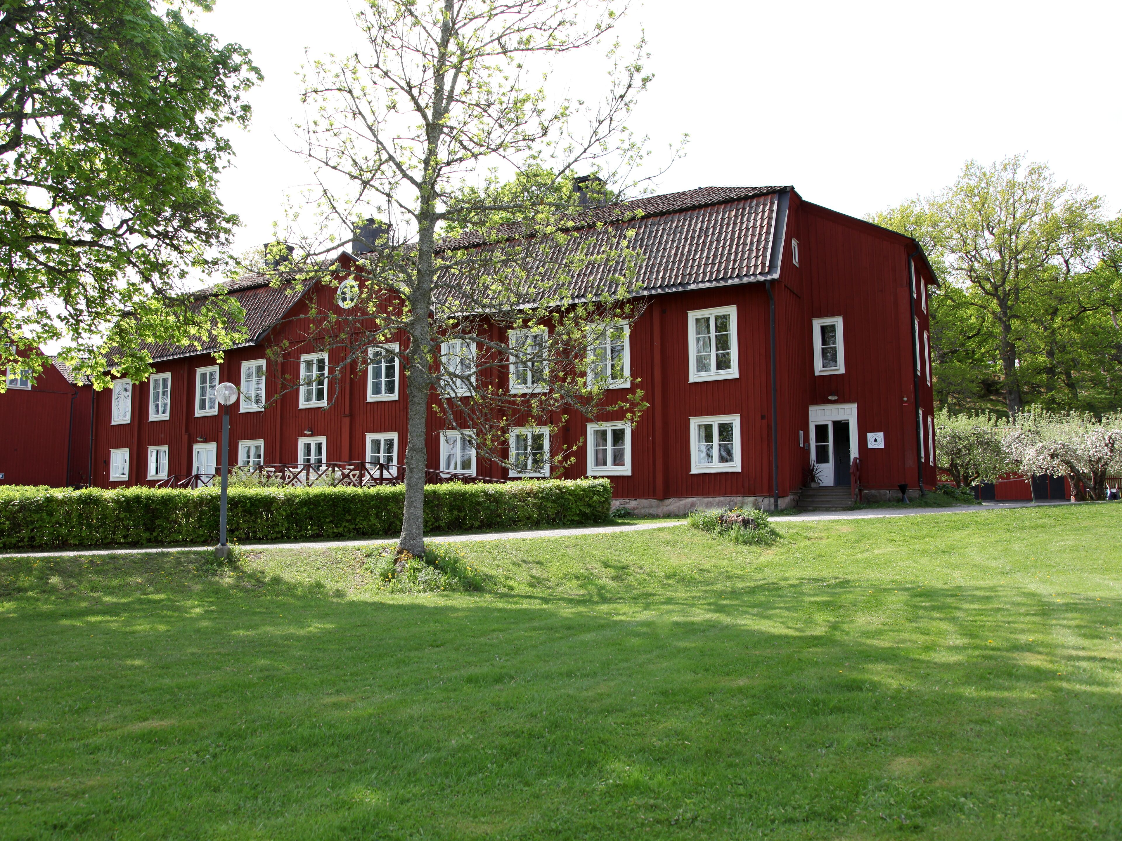 Punainen rakennus, jossa on useita ikkunoita ja hyvin hoidettu nurmikko.