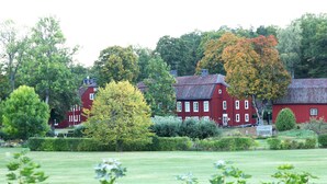 A red building with multiple windows and a chimney, surrounded by lush greenery and trees. - Gripsholms Bed & Breakfast (Mariefred)