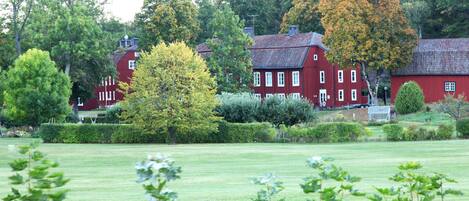 A red building with multiple windows and a chimney, surrounded by lush greenery and trees.