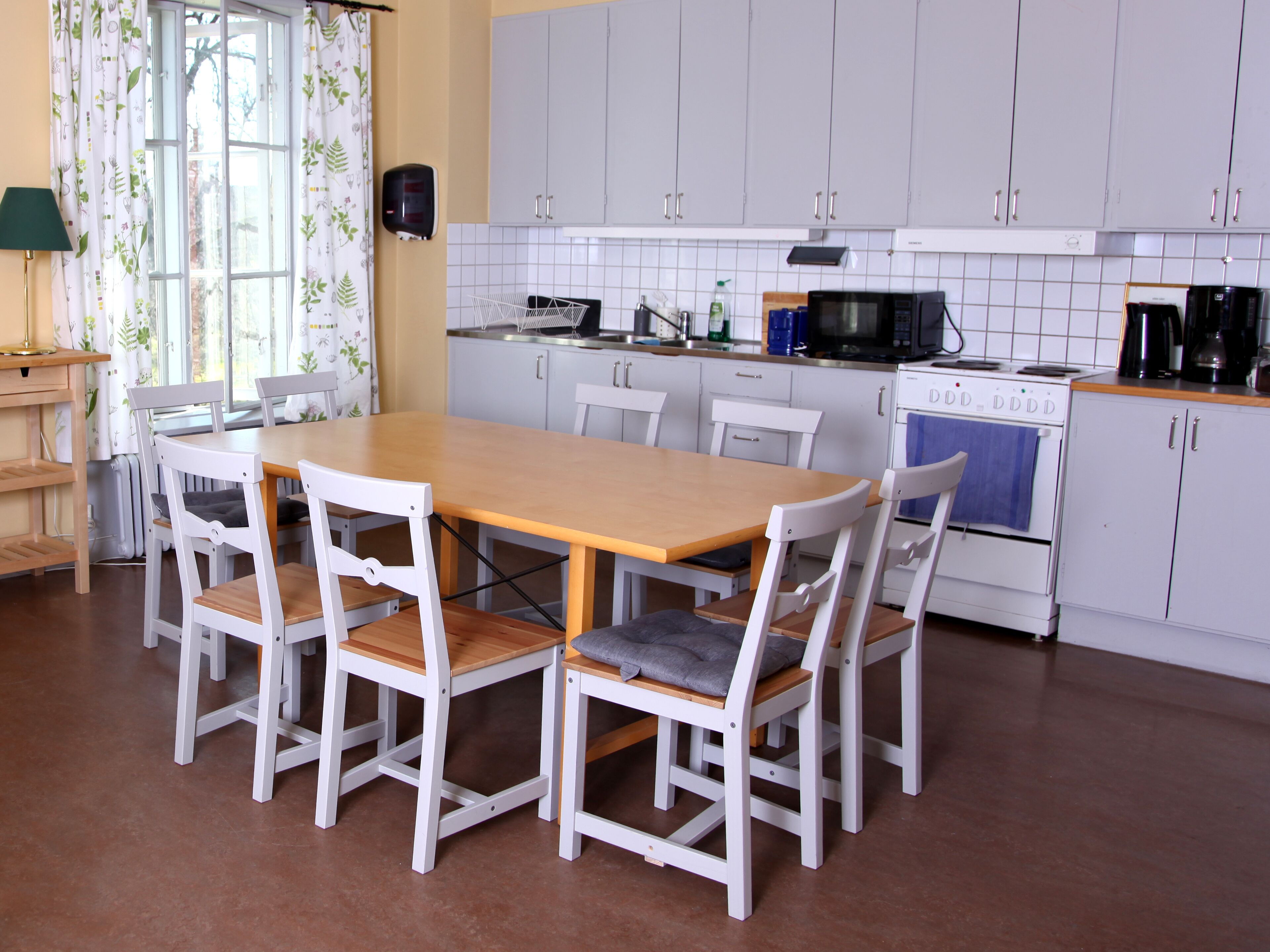A kitchen with a wooden table and white chairs, white cabinets, a stove, and a microwave.