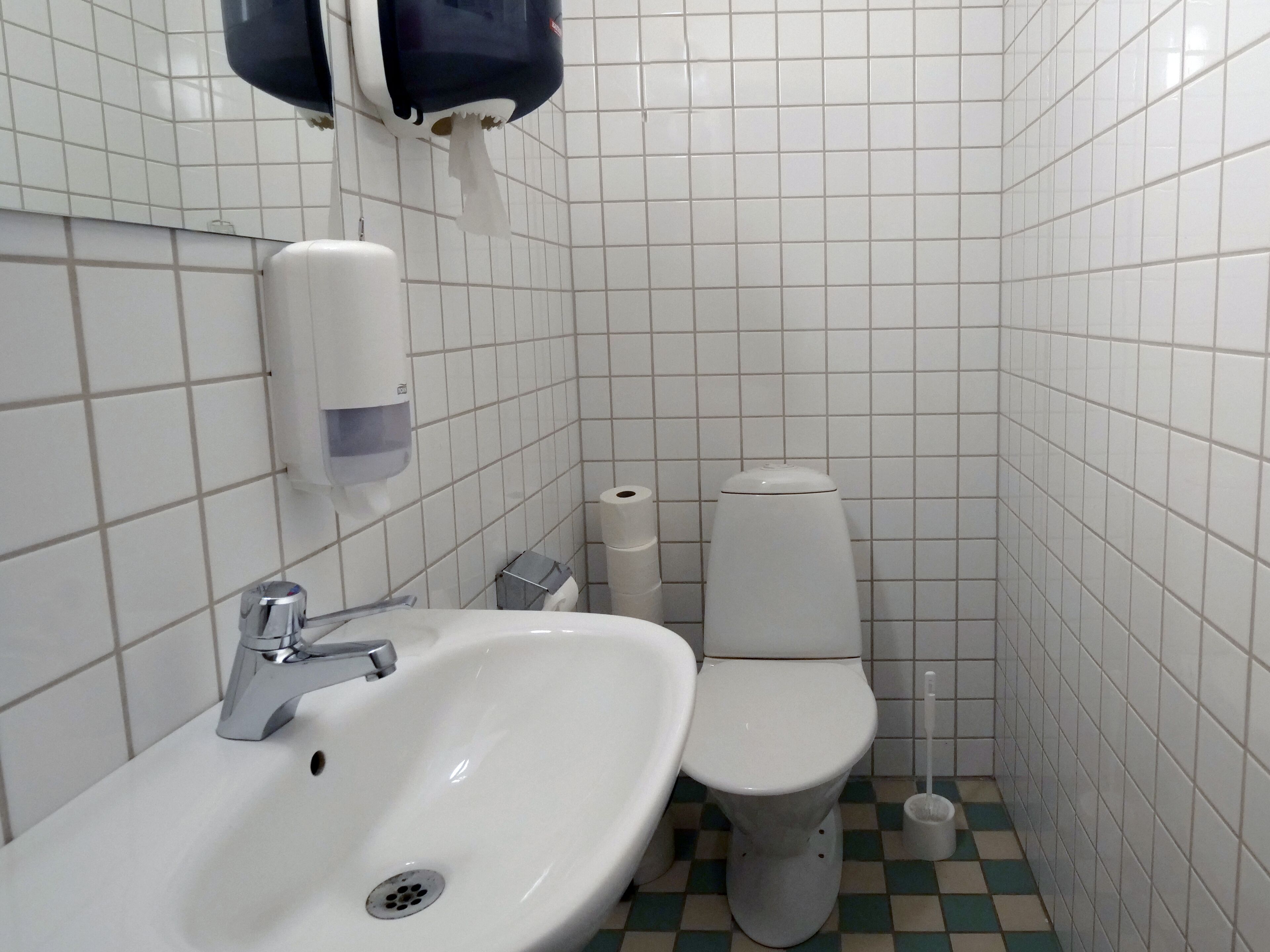 Une petite salle de bain avec un lavabo blanc, des toilettes et un distributeur de serviettes en papier.