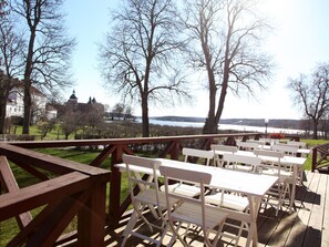 A wooden deck with white picnic tables and benches overlooking a body of water and a distant building. - Gripsholms Bed & Breakfast (Mariefred)