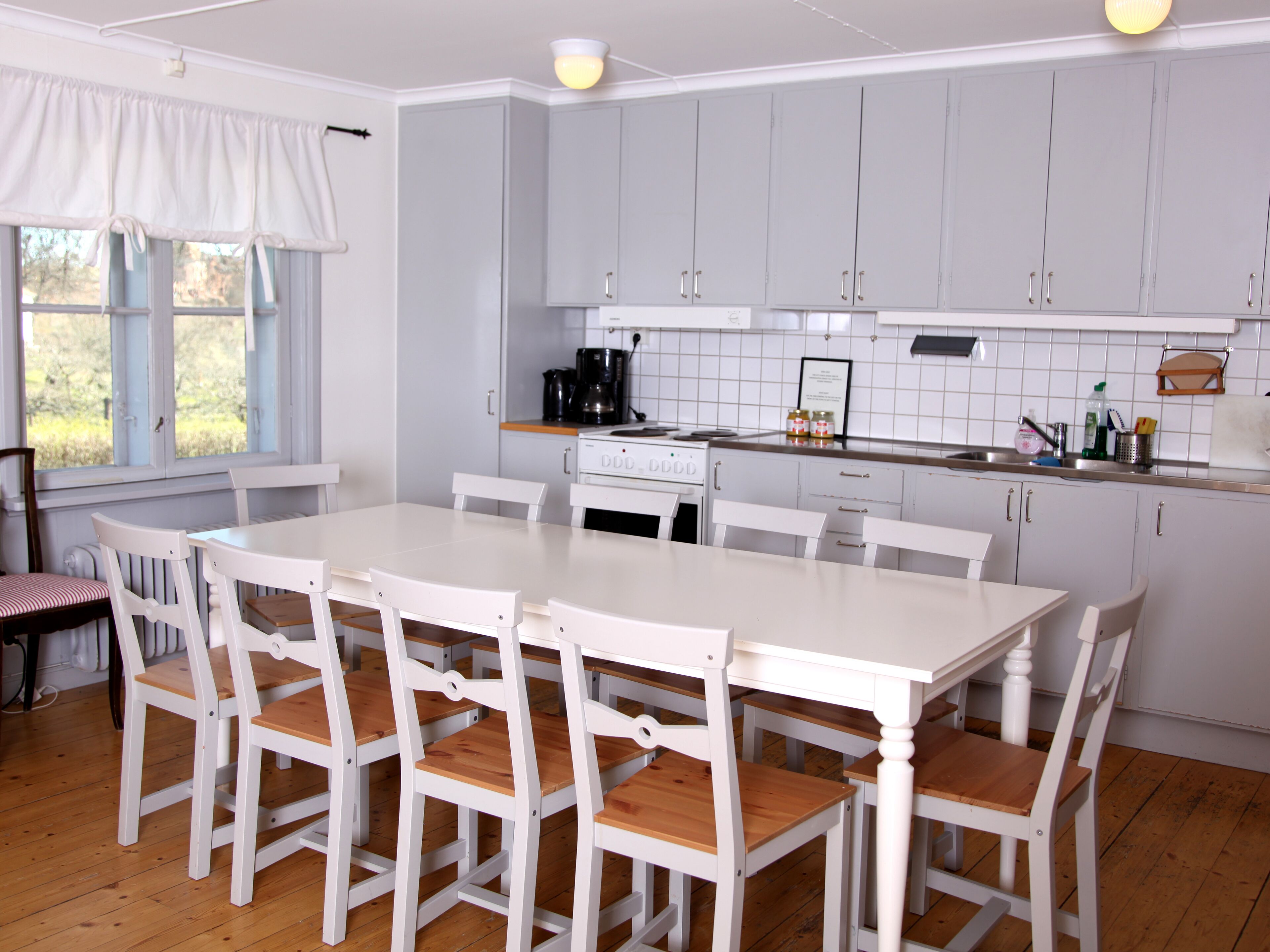 Una cocina con armarios blancos, una mesa de comedor blanca y sillas de madera.