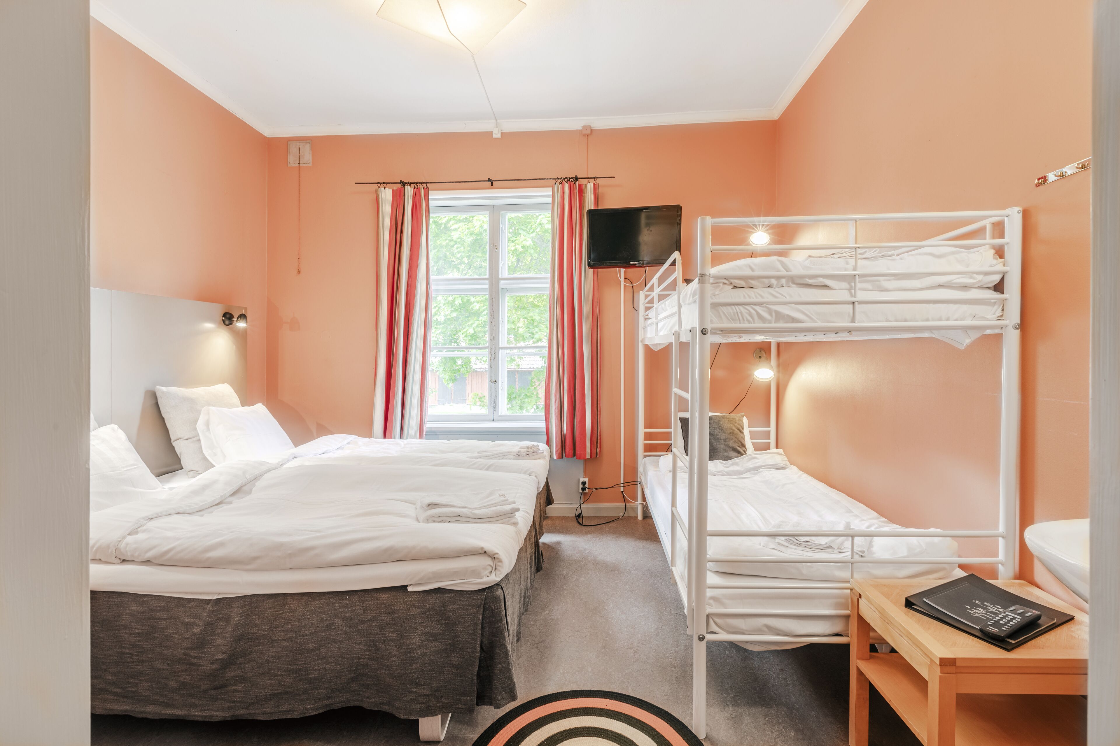 A room with two beds, a TV, and a window with curtains.