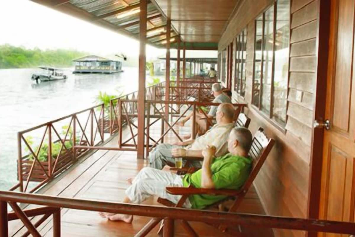 A wooden deck with a railing overlooking a river, with a boat visible in the distance.