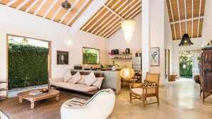 A spacious living area with a high ceiling, a sofa, a coffee table, and a dining area with a lamp. - Villa 007 (Seminyak)