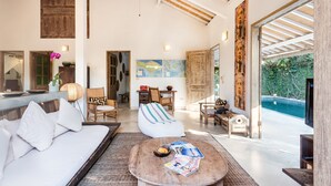 A spacious living area with a large sofa, a round coffee table, and a view of a swimming pool. - Villa 007 (Seminyak)