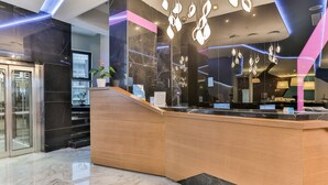 A modern reception area with a marble floor, a wooden reception desk, and contemporary lighting fixtures. - Hotel Bracera (Budva)