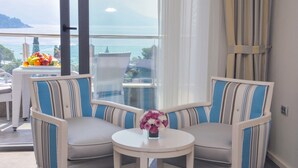 A balcony with a view of the sea and mountains, two striped chairs, a small table with a vase of flowers, and a fruit basket. - Hotel Bracera (Budva)