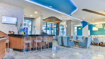 Un moderno vestíbulo de hotel con área de bar, asientos y ventanas amplias.