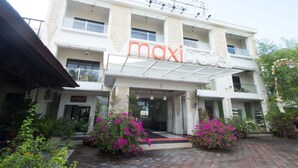 Un immeuble à plusieurs étages, sur lequel on peut lire les inscriptions « maxi hôtel » et « grand magasin », et un tapis rouge menant à l’entrée.