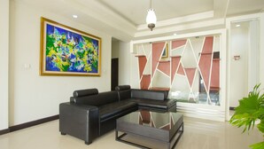 Un salon moderne avec un canapé d’angle noir, une table basse en verre et un grand tableau abstrait accroché au mur.