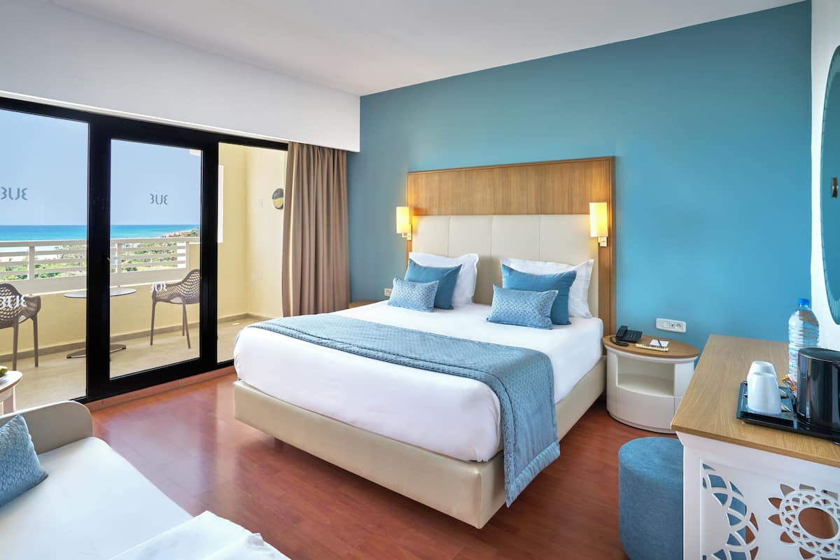 Habitación de hotel con una cama grande, un escritorio, una silla y vista a la playa.