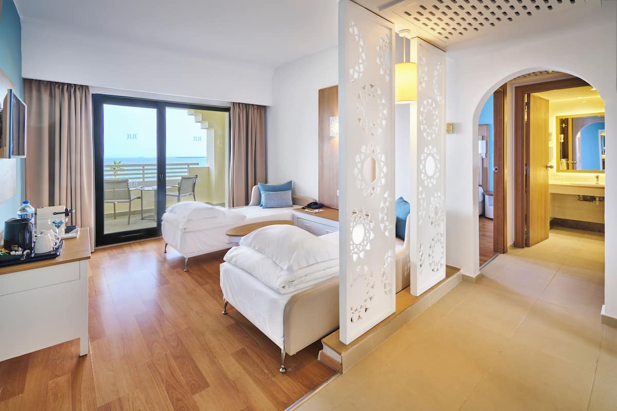 Una habitación de hotel con dos camas, un balcón, zona de comedor y baño.