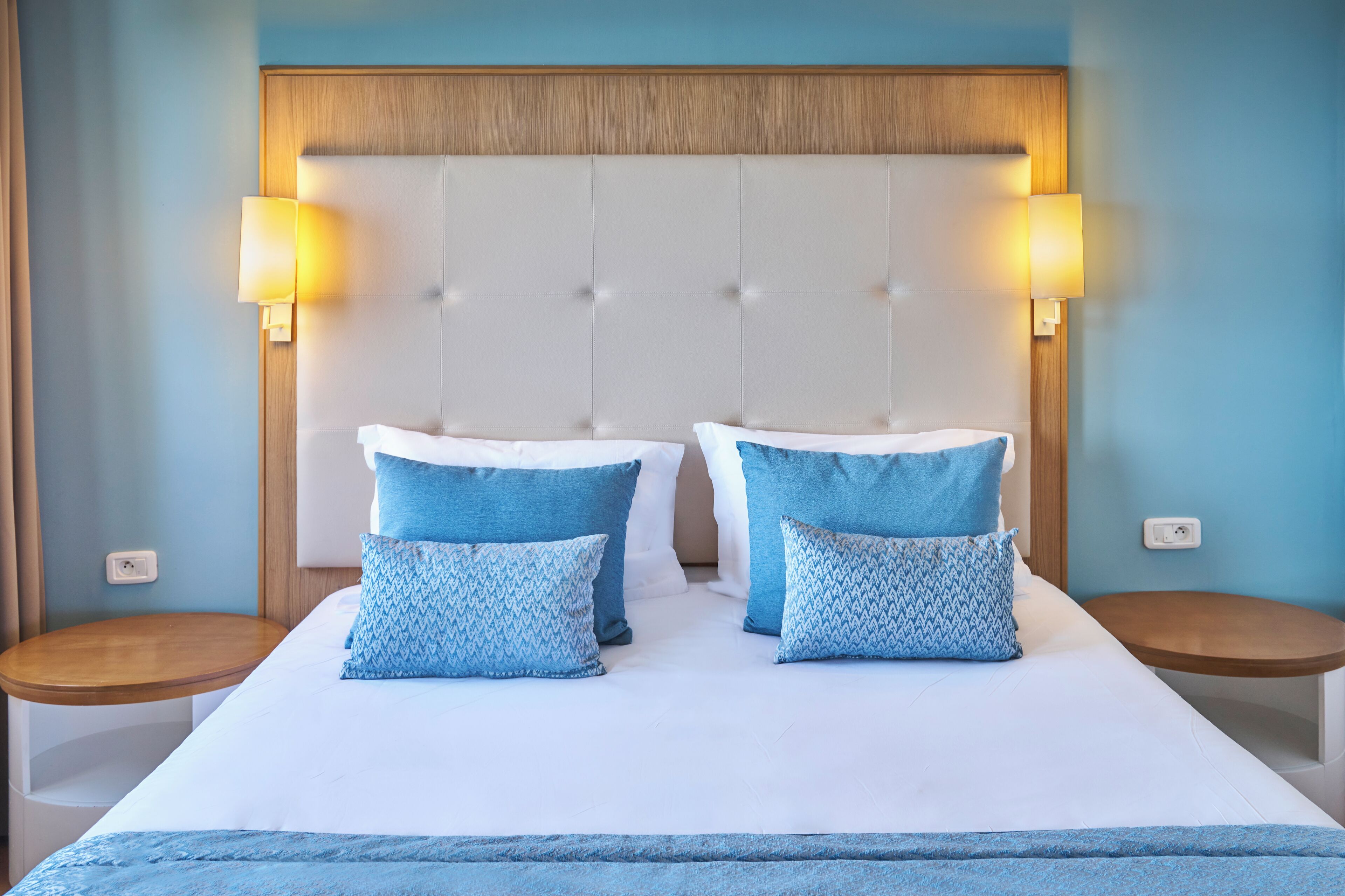 A hotel room with a large bed, two bedside tables, and a headboard with a light wood finish.