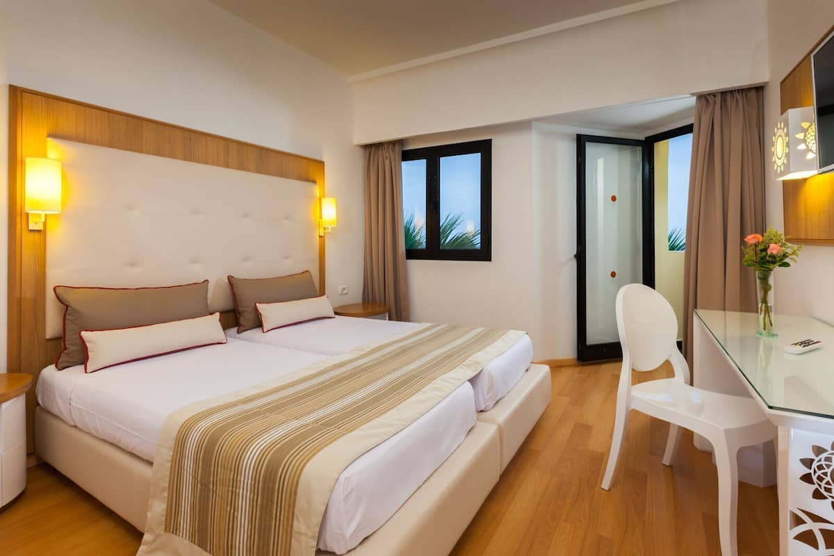 Habitación de hotel con una cama grande, lámparas de noche, un escritorio con silla y vistas por una puerta.