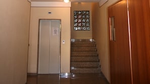 A staircase with a wooden handrail, a chandelier, and a door at the bottom. - Residenza Novalba (Riccione)