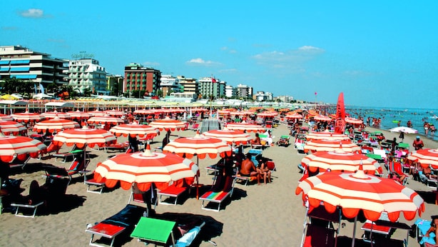 A beach with numerous red and white striped umbrellas and beach chairs, indicating a sunny day at a public beach area. - Residenza Novalba (Riccione)