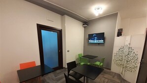 A small, modern room with a wooden herringbone floor, a flat-screen TV mounted on the wall, a small table with two chairs, and a door with frosted glass. - Casa Provenza Rooms (Catania)