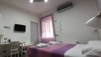Una camera d'albergo con un letto, una scrivania, una sedia, una televisione e una finestra con tende.