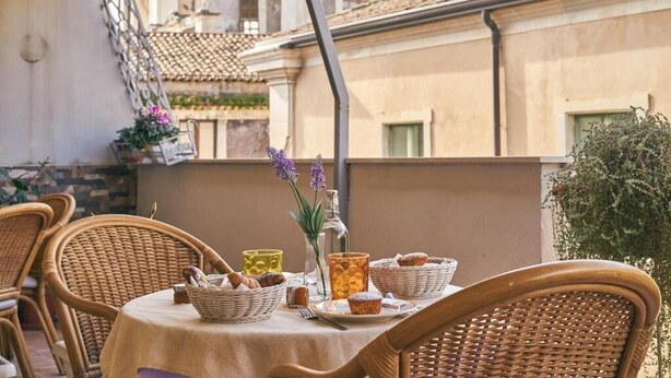 A table set with wicker chairs, baskets, and a vase with flowers. - Casa Provenza Rooms (Catania)