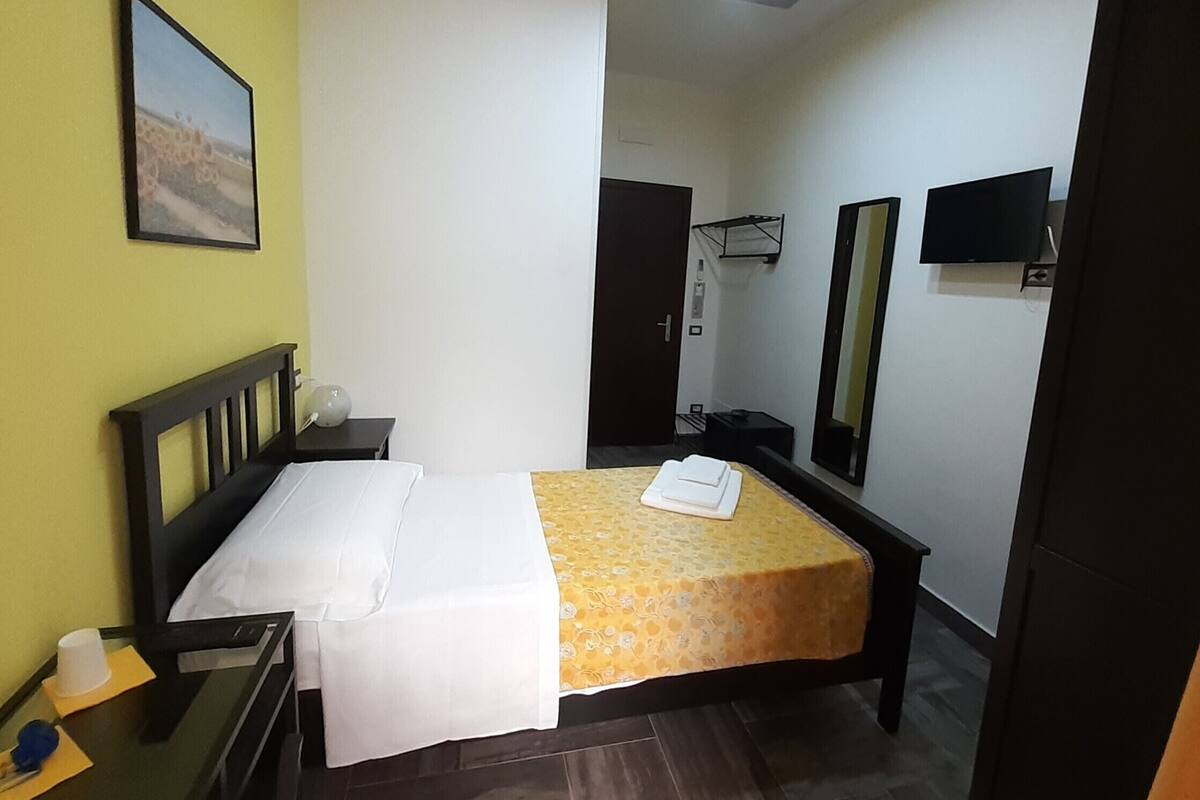A hotel room with a bed, a bedside table, a chair, a television, and a mirror.