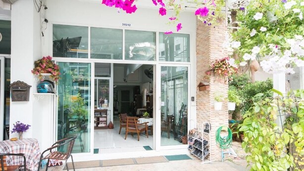 Fachada com uma grande porta de vidro, parede de tijolos e flores penduradas.