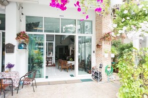 A storefront with a large glass door, a brick wall, and hanging flowers. - Admire House (Pattaya)
