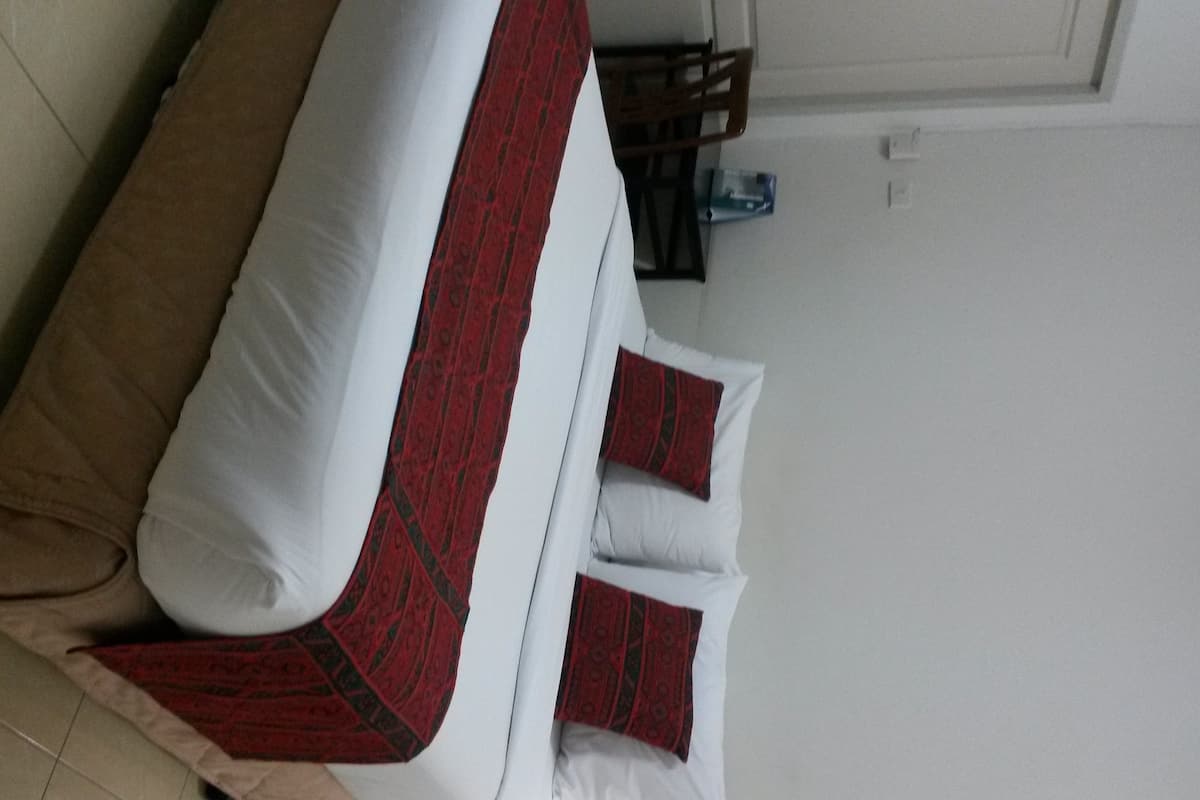 A bed with a beige cover, white pillows, and a red and black patterned bedspread.