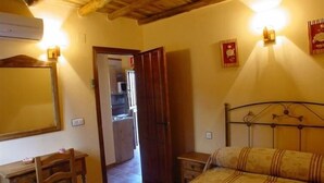 A bedroom with a wooden bed, a desk with a chair, a wardrobe, and a small bedside table.