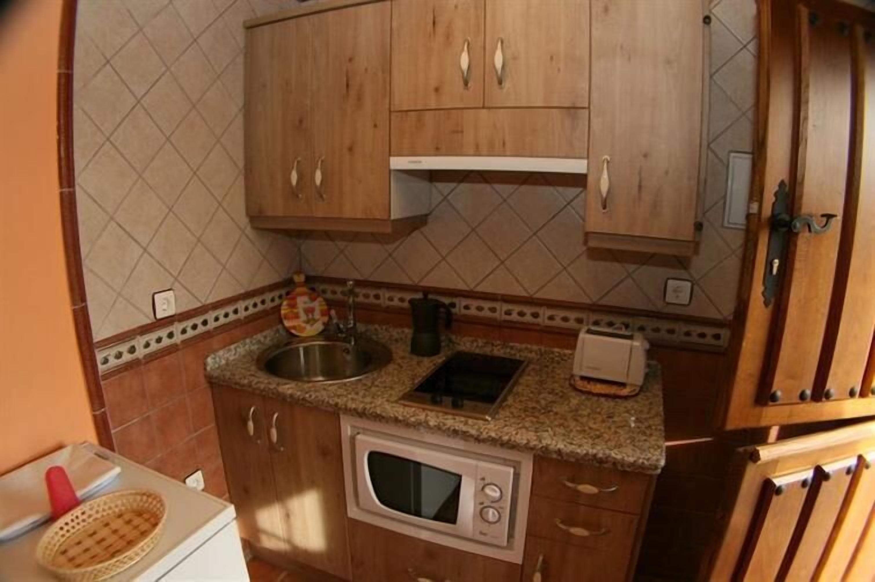 Una cocina compacta con muebles de madera, microondas, fregadero y tostadora.
