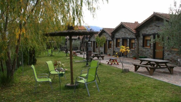 A courtyard with stone buildings, green chairs, picnic tables, and a pergola.