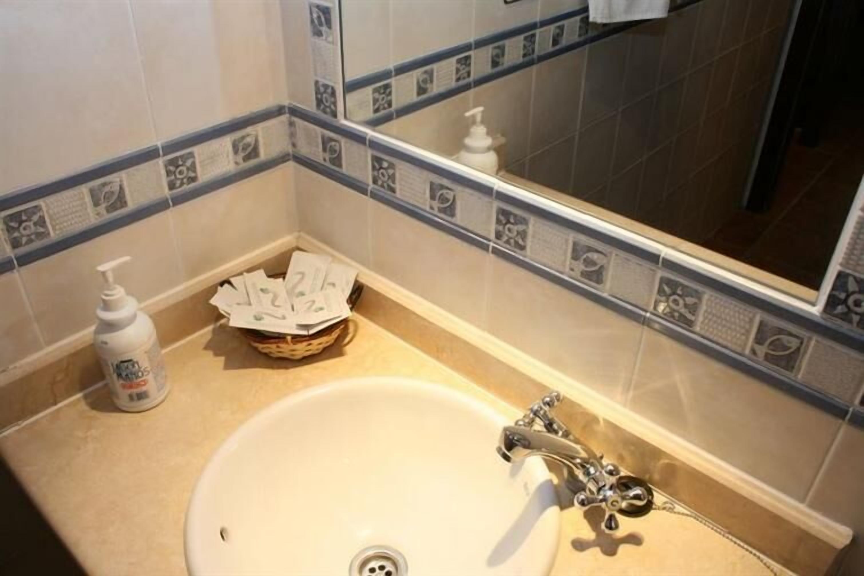 Un baño con lavamanos, espejo y artículos de aseo.