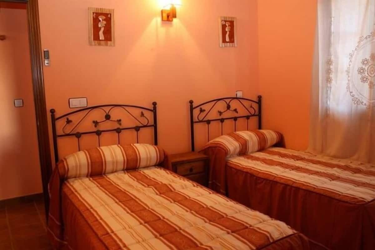 A room with two beds, each with striped bedding, a nightstand, and wall-mounted light fixtures.