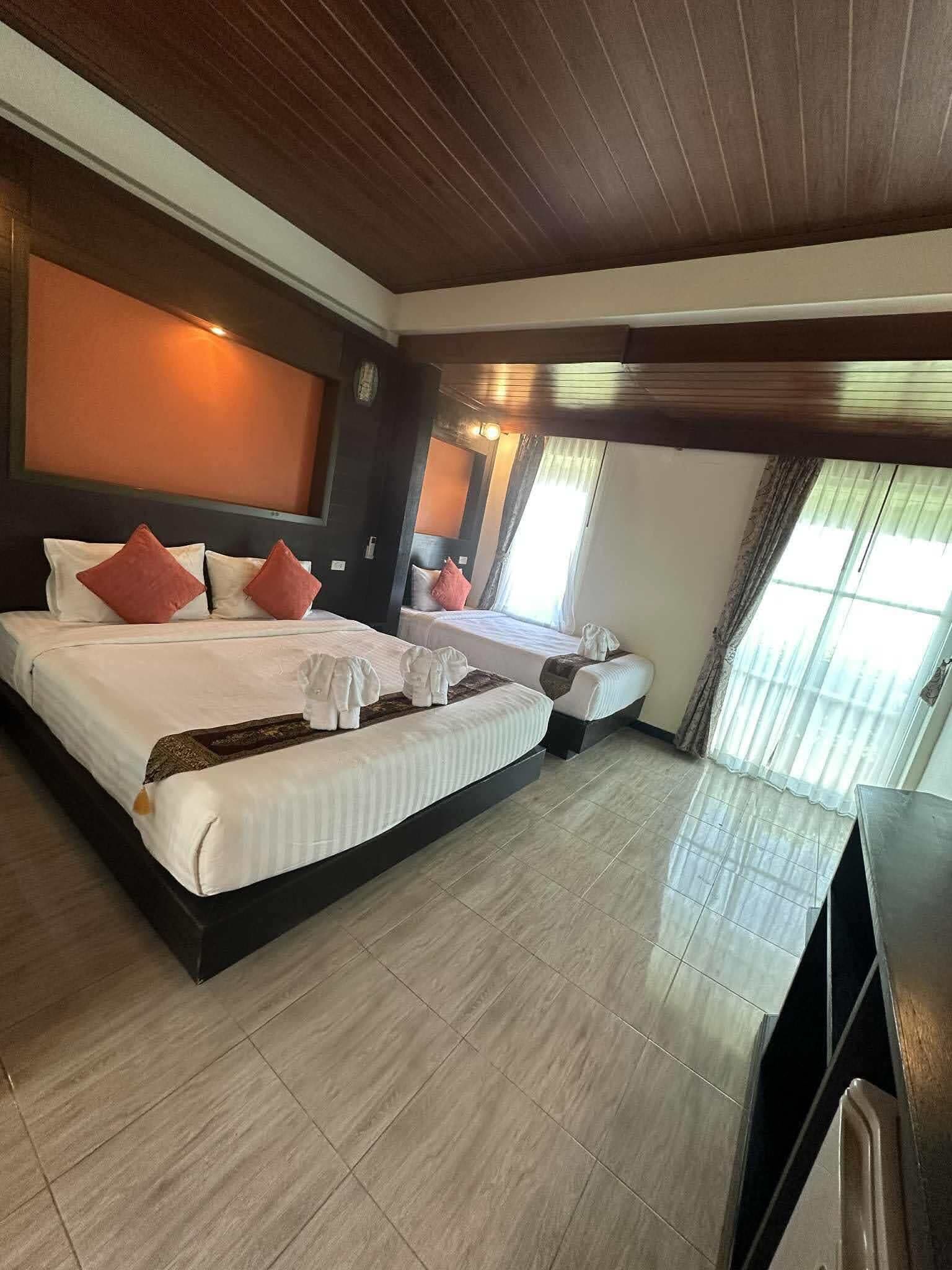 A hotel room with two beds, a wooden ceiling, and a large window with curtains.