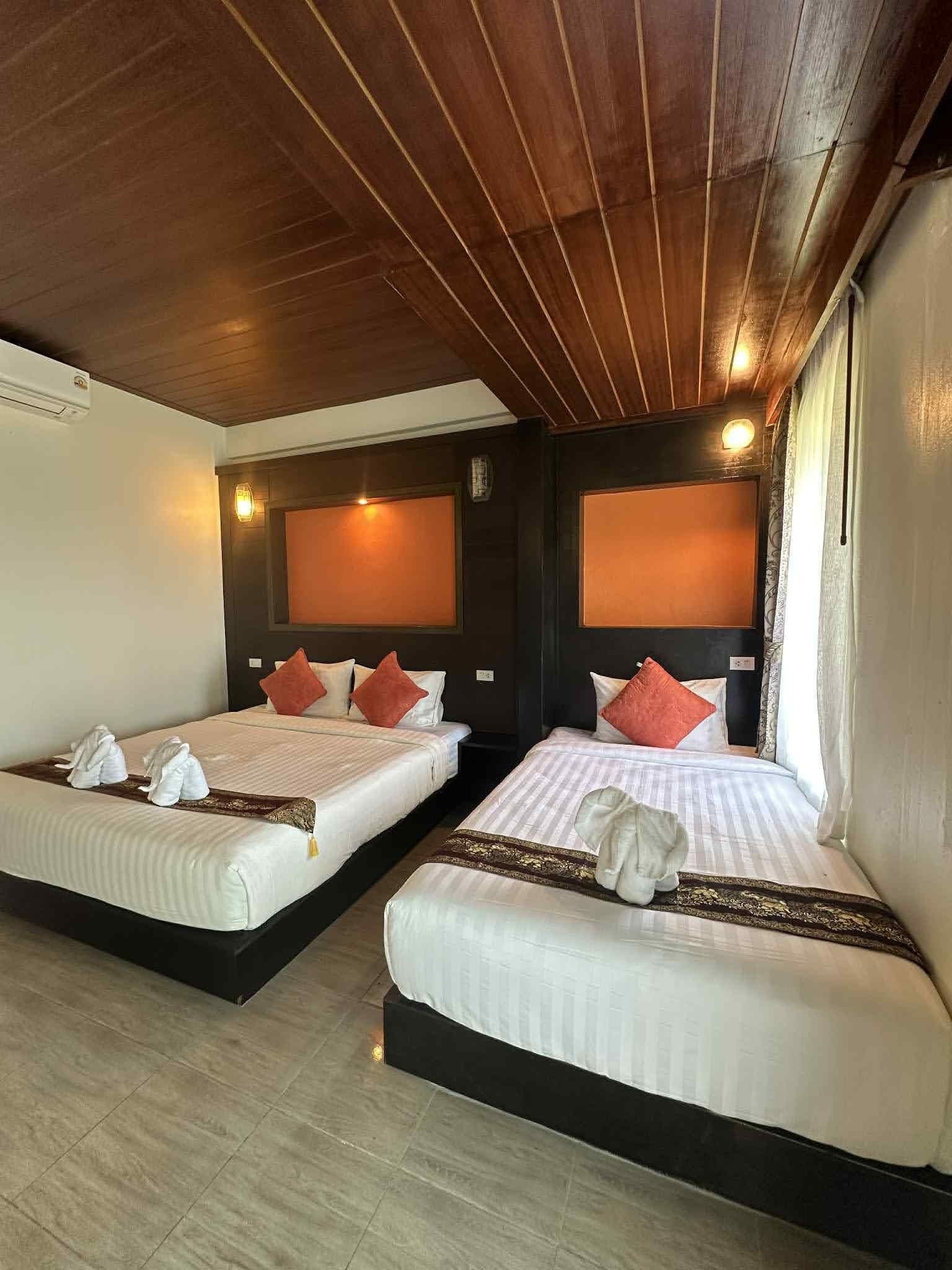 A hotel room with two beds, wooden ceiling, and a window with curtains.