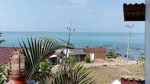 A coastal view with a clear sky, a beach with rocks, and a few houses. - The Sea At Lanta Hotel (Ko Lanta)