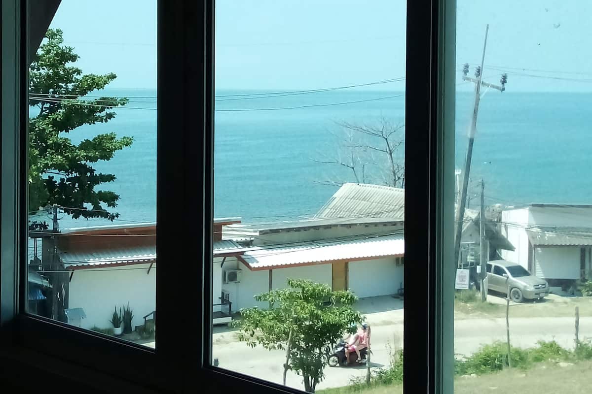 A view through a window with a view of the sea and a building with a red roof.