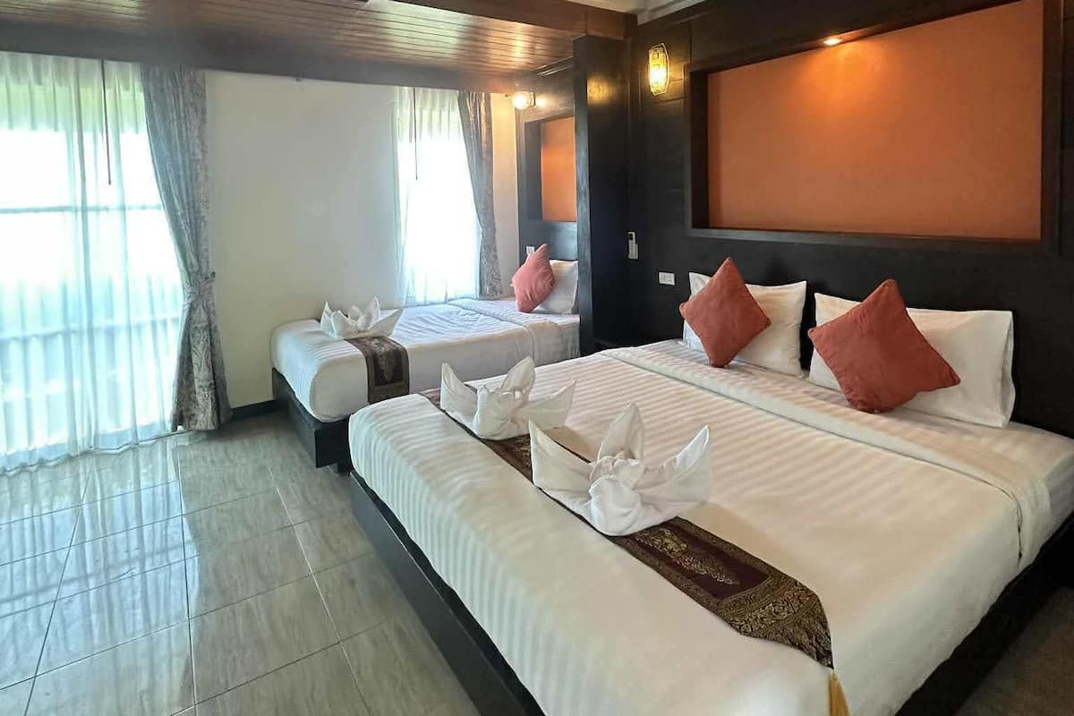 A hotel room with a large bed, two smaller beds, a sitting area, and a large window with curtains.