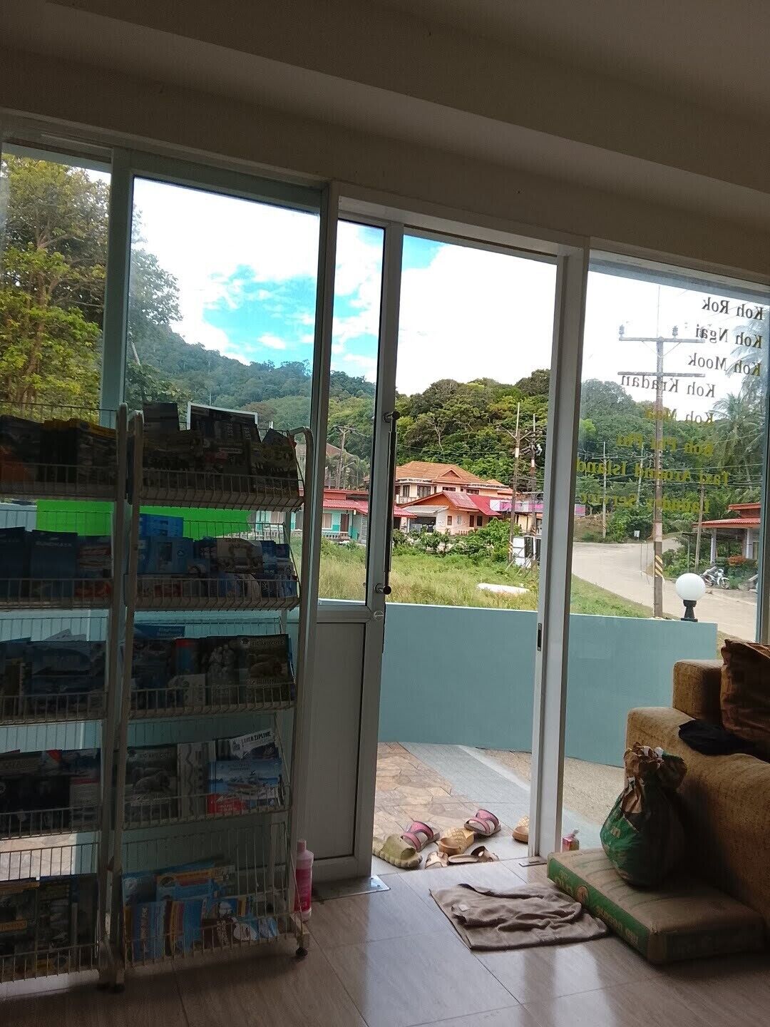 A room with a large sliding glass door leading to a balcony, a small seating area with a cushion, and a shelf with various items.
