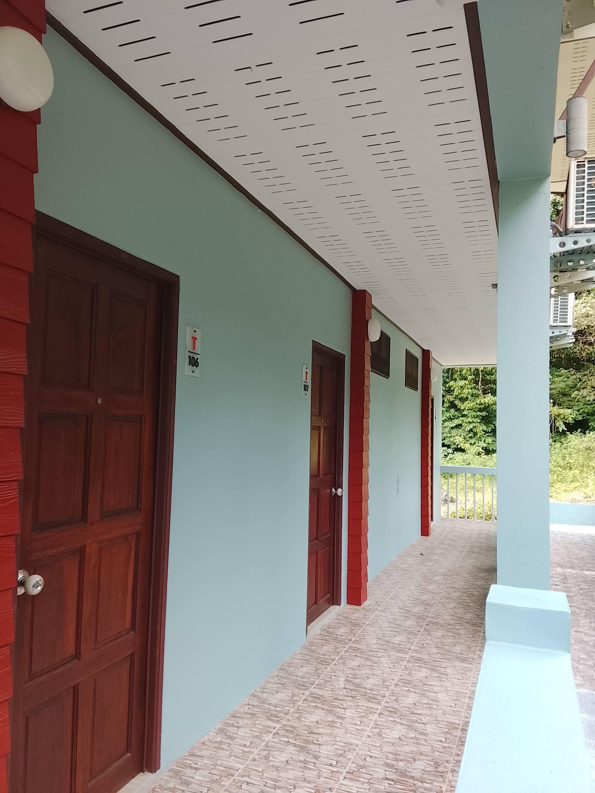 Un couloir avec des portes en bois, un sol carrelé et un plafond équipé d’un système de ventilation.