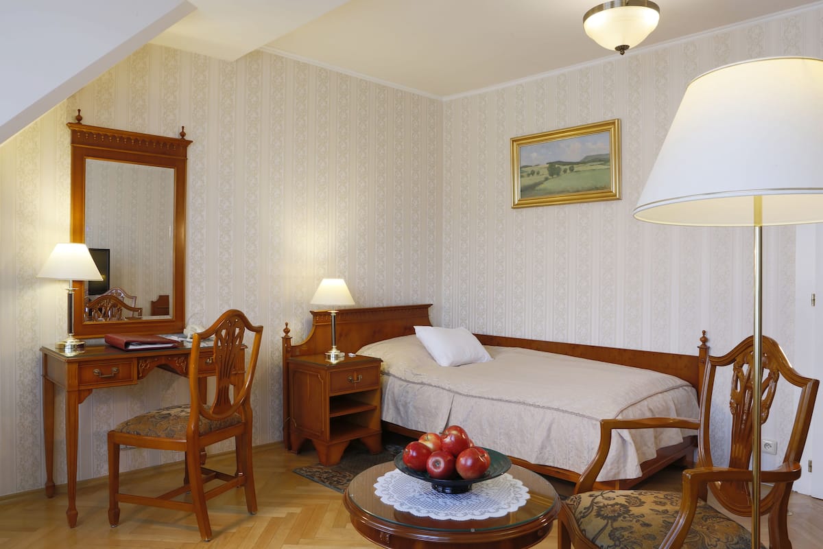 Ein Hotelzimmer mit einem Bett, zwei Stühlen, einem Schreibtisch mit Lampe, einem Spiegel und einem Tisch mit Äpfeln.