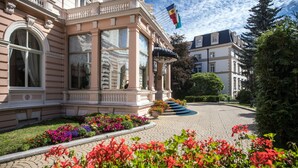 Un bâtiment historique doté d’une entrée imposante, de grandes fenêtres et d’un jardin bien entretenu, agrémenté de fleurs aux couleurs vives.