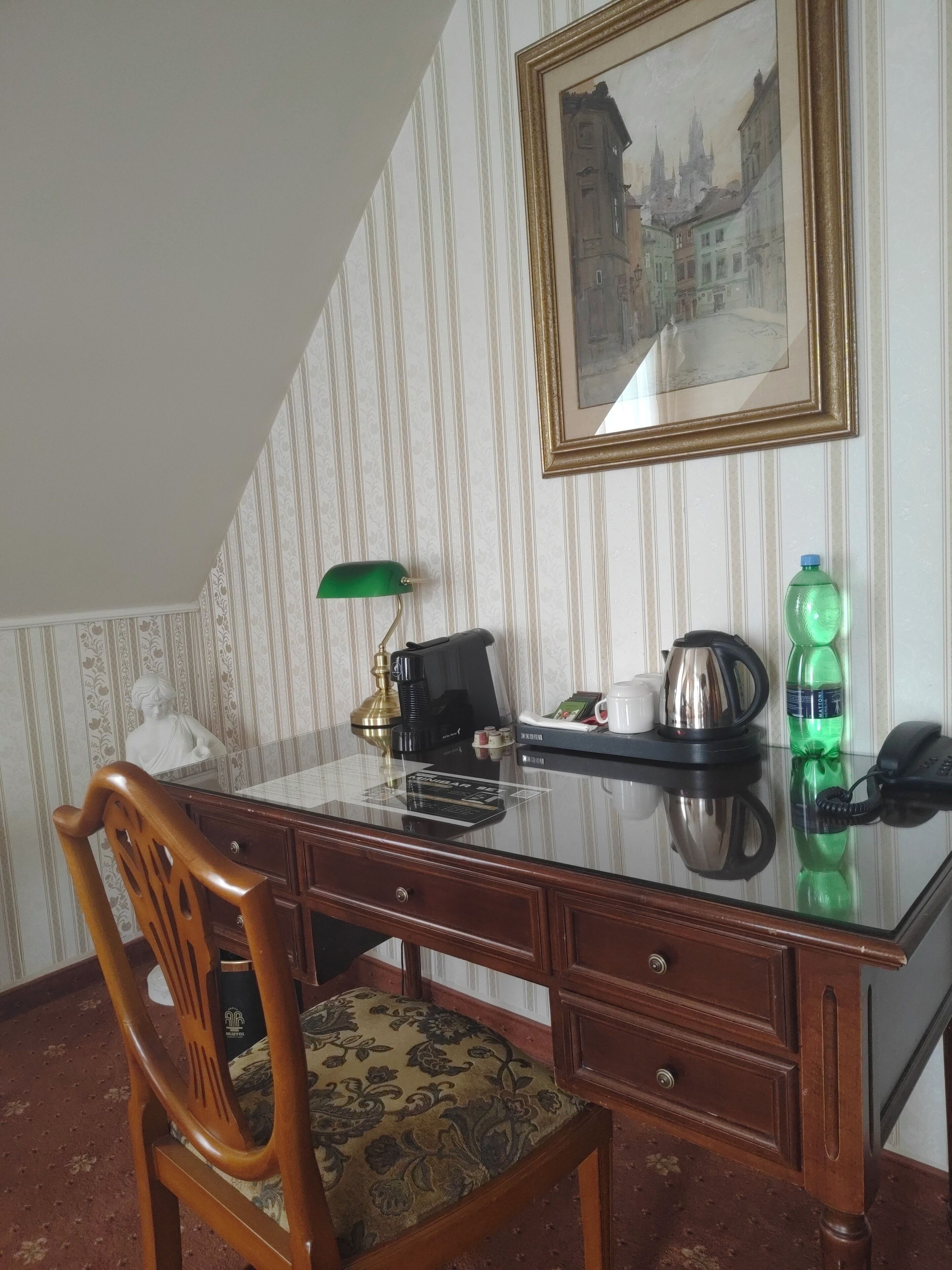 Una habitación con un escritorio de madera, una silla, un cuadro en la pared, una botella verde y un teléfono.